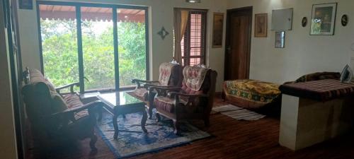 a living room with chairs and a table and windows at East West Farm Homestay in Munnar