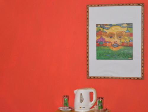 a picture hanging on a red wall with a coffee maker at Namaste Yoga Farm in Gokarna