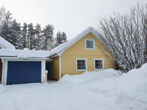 a yellow house with a blue garage in the snow at Villa Hugo in Vidsel