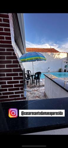 a table and chairs under an umbrella next to a pool at Recanto Mãe Aparecida in Aparecida