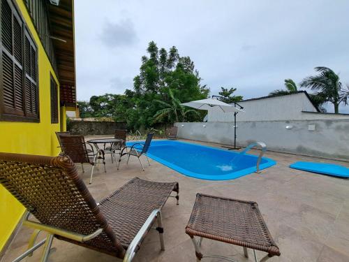 a swimming pool with chairs and a table and an umbrella at Casa com Piscina, Churrasqueira e Quadra de Vôlei! in Pontal do Paraná