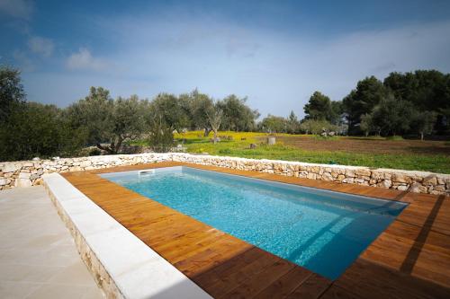 een zwembad met een houten terras en een stenen muur bij Trulli Magda in Martina Franca