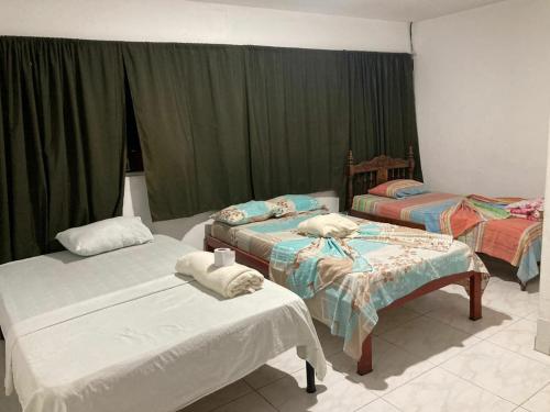 two beds in a room with green curtains at Hotel y restaurante juanchito in Pitalito