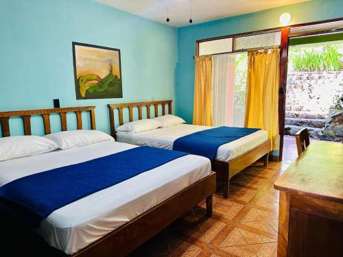 two beds in a room with blue walls and a window at Lake Arenal Hotel & Brewery in Tilarán