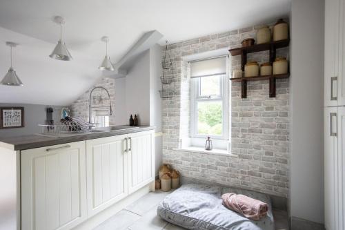 a kitchen with white cabinets and a brick wall at Cosy, tranquil, fully equipped & beautiful garden - Dene Cottage in Newham