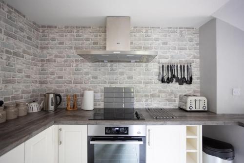 a kitchen with white cabinets and a brick wall at Cosy, tranquil, fully equipped & beautiful garden - Dene Cottage in Newham
