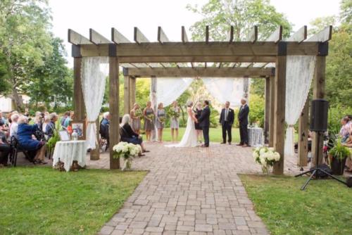a bride and groom standing under an outdoor altar at Fairholm Boutique Inns in Charlottetown