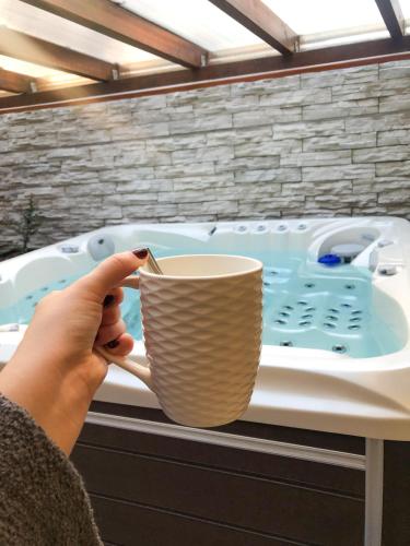 a person holding a cup in front of a bath tub at Zengő Kincse SPA Vendégház Hosszúhetény in Hosszúhétény