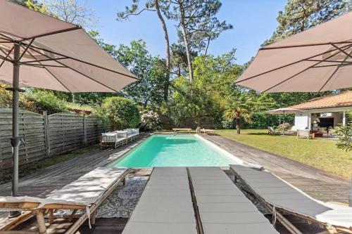 une piscine avec chaises et parasols dans une cour dans l'établissement Villa bohème chic avec piscine & jardin au Pyla, à La Teste-de-Buch