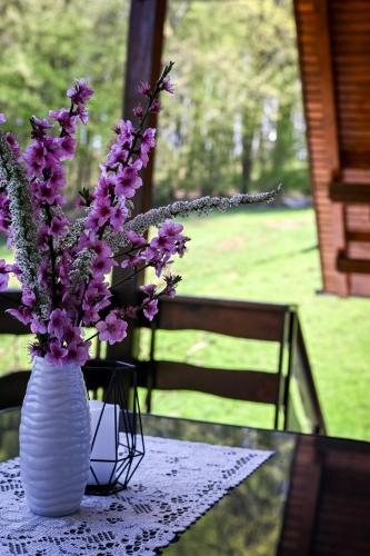 a white vase with purple flowers on a table at Countryside house in Male Brusnice