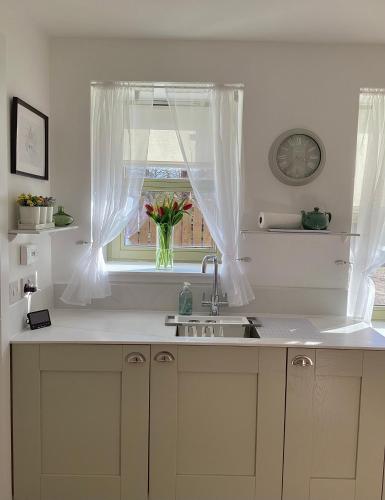a kitchen with a sink and a window with a vase of flowers at Cottage in Mid Calder Village near Edinburgh in Mid Calder