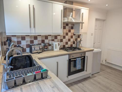 a kitchen with white cabinets and a stove top oven at Ty Collective - Near Town Centre in Dowlais