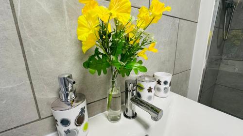 a vase of yellow flowers sitting on a bathroom sink at Cosy and Comfy Deluxe Entire Apartment in London