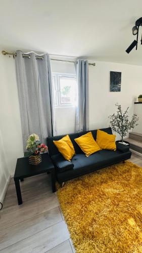 a black couch with yellow pillows in a living room at Cosy and Comfy Deluxe Entire Apartment in London