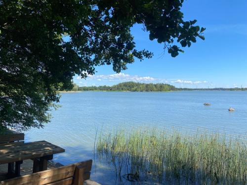 a view of a lake with a wooden bench at Kolme makuuhuonetta Merenrannalla Lauttasaaressa in Helsinki
