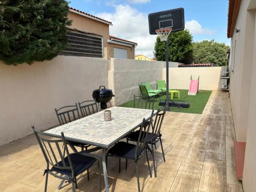 une terrasse avec une table et des chaises ainsi qu'un panier de basket-ball. dans l'établissement Villa dans le sud de la France, à Baixas