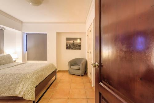 a bedroom with a bed and a chair and a door at Escape 3BR Apartment Close to Downtown Mall in Bella Vista in Santo Domingo
