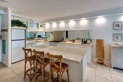 a kitchen with white cabinets and a island with two chairs at Poinciana 012 & Free Buggy Hamilton Island in Hamilton Island