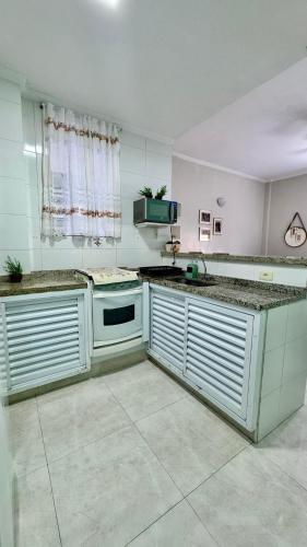 a large kitchen with white cabinets and a sink at Studio 511 Pitangueiras - na quadra da praia in Guarujá
