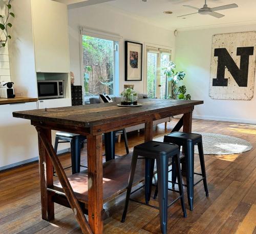 a large wooden table in a living room with stools at Welcome to The Roy - Family home close to airport and train! in Melbourne