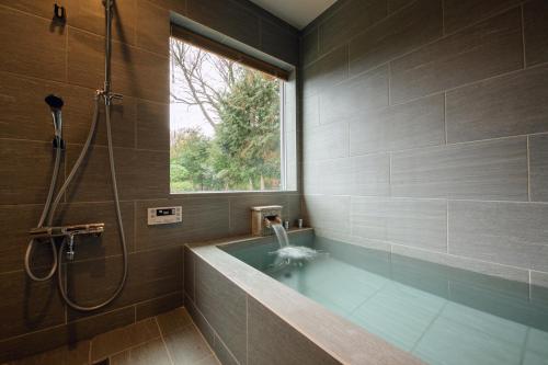 ein Bad mit einer Badewanne und einer Dusche mit einem Fenster in der Unterkunft Hakone Ninotaira Cottage in Onsensō