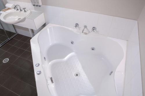 a white bath tub in a bathroom with a sink at Balan Village Motel in Nowra