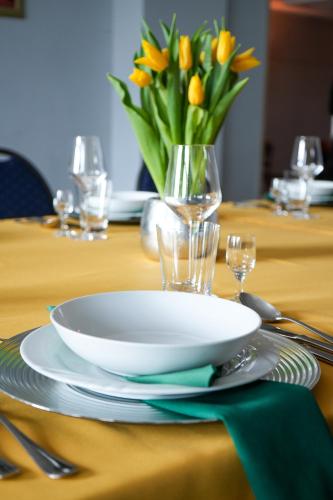 a table with a plate and a vase of yellow flowers at Hotel Festival in Opole