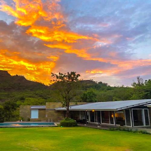 a building in a field with a sunset in the sky at Dharana at Shillim All Inclusive Luxury Wellness Retreat in Lonavala