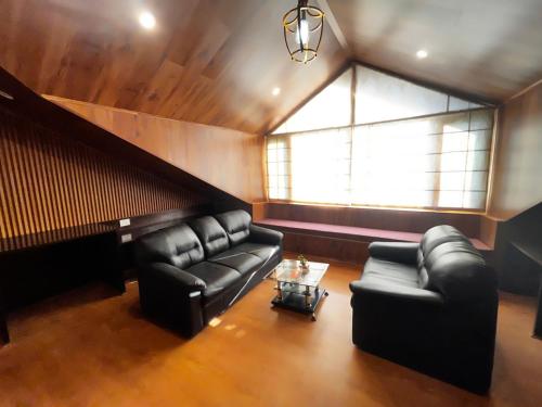 a living room with black leather furniture and a window at Jubilant Farm House in Rishīkesh