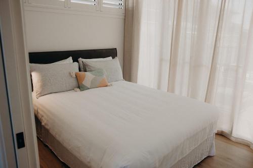 - un lit avec des draps et des oreillers blancs à côté d'une fenêtre dans l'établissement Dudley Villa, à Evans Head