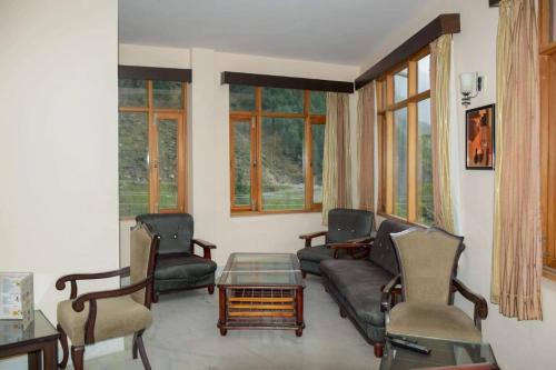 a living room with a couch and chairs and windows at Red Inn in Vashisht