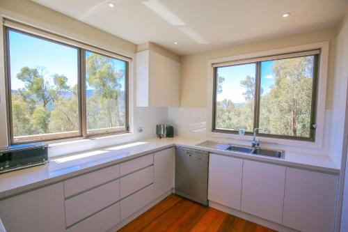 a kitchen with white cabinets and two windows at Kangaroo Lodge in Bright