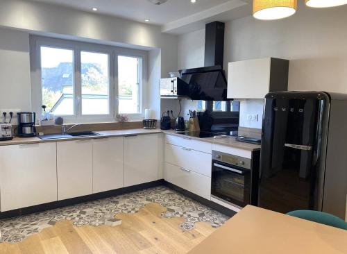 une cuisine avec des armoires blanches et un réfrigérateur noir dans l'établissement Maison à 250m de la plage la Grève Blanche avec WIFI à TREGASTEL - Réf 182, à Trégastel