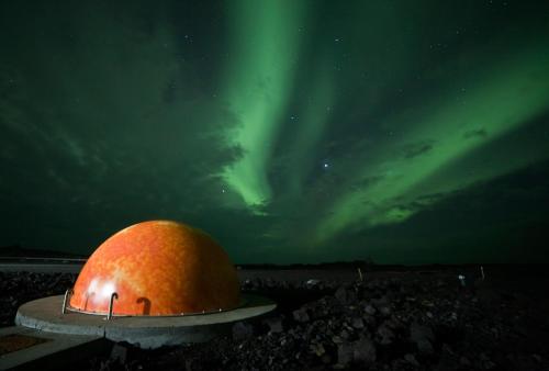 an orange observatory with the aurora in the background at The Apartment at Reykjanesviti in Hafnir