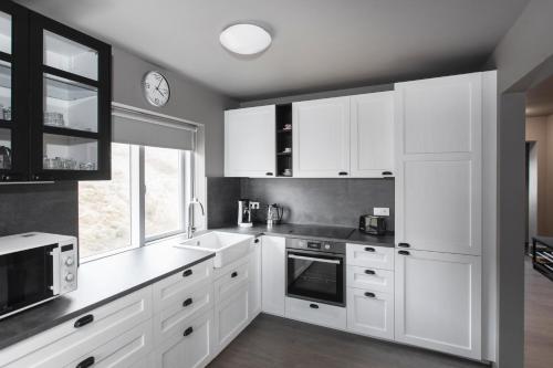 a kitchen with white cabinets and a clock on the wall at The Apartment at Reykjanesviti in Hafnir