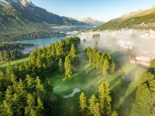 an aerial view of a golf course in the mountains with fog at Kulm Hotel St. Moritz in St. Moritz