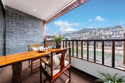 a balcony with a wooden table and a view of the ocean at Jiuqi Tongnian High-end River View B&B in Fenghuang