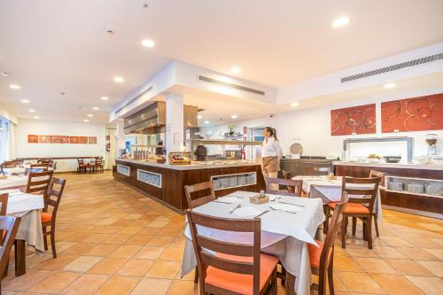 Un restaurante con mesas y una persona de pie en la cocina. en Aparthotel Holiday Center, en Santa Ponsa