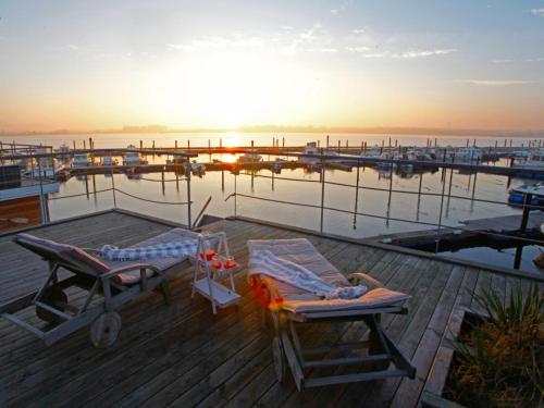 twee mensen op ligstoelen op een steiger met een jachthaven bij Hausboot Poseidon 1 in Großenbrode