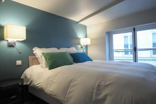 une chambre avec un grand lit blanc avec des oreillers verts dans l'établissement Molière ChicSuites, à Paris