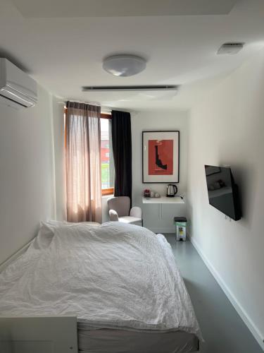 a white bedroom with a bed and a chair at Oasis Airport Apartments and Rooms in Velika Gorica