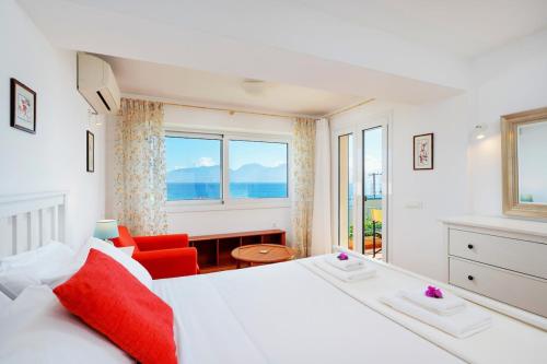 a bedroom with a large white bed and a red chair at Idyllic Beachfront House in Agios Nikolaos