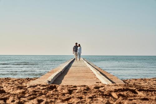 two people walking on a wooden pier over the water at Falkensteiner Hotel & Spa Jesolo in Lido di Jesolo