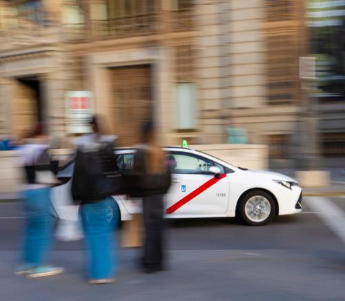 a white car driving down a city street with people at Hotel Regina in Madrid