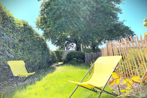 deux chaises jaunes assises dans l'herbe près d'une clôture dans l'établissement La Balise-Appart dans un manoir-Vue mer et jardin, à La Terre du Pont