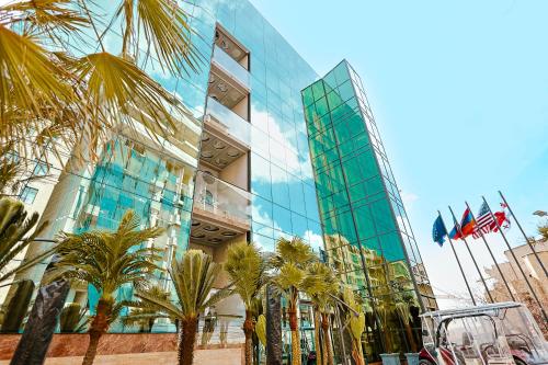a glass building with palm trees in front of it at Carat Hotel Yerevan in Yerevan
