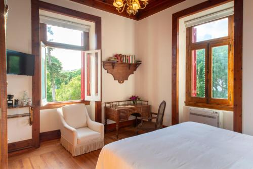 a bedroom with a bed and a desk and windows at Chalet Ficalho in Cascais