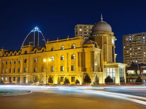 a yellow building with a clock tower in front of buildings at The Central Point Hotel Baku in Baku