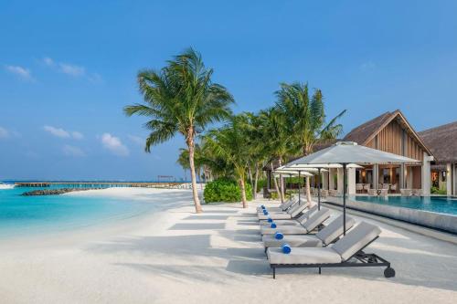 a row of lounge chairs on a beach at JW Marriott Maldives Kaafu Atoll Island Resort in Male City