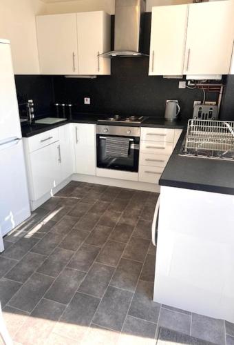 a kitchen with white cabinets and a tile floor at Kelpies Serviced Apartments Hamilton- 2 Bedrooms in Falkirk